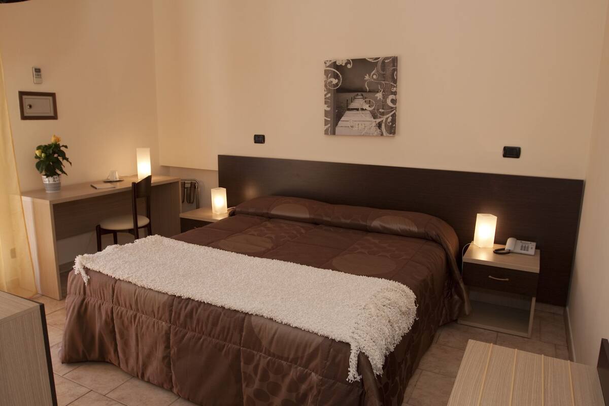 Ein Hotelzimmer mit einem großen Bett, Nachttischen mit Lampen, einem Schreibtisch und einem Stuhl.