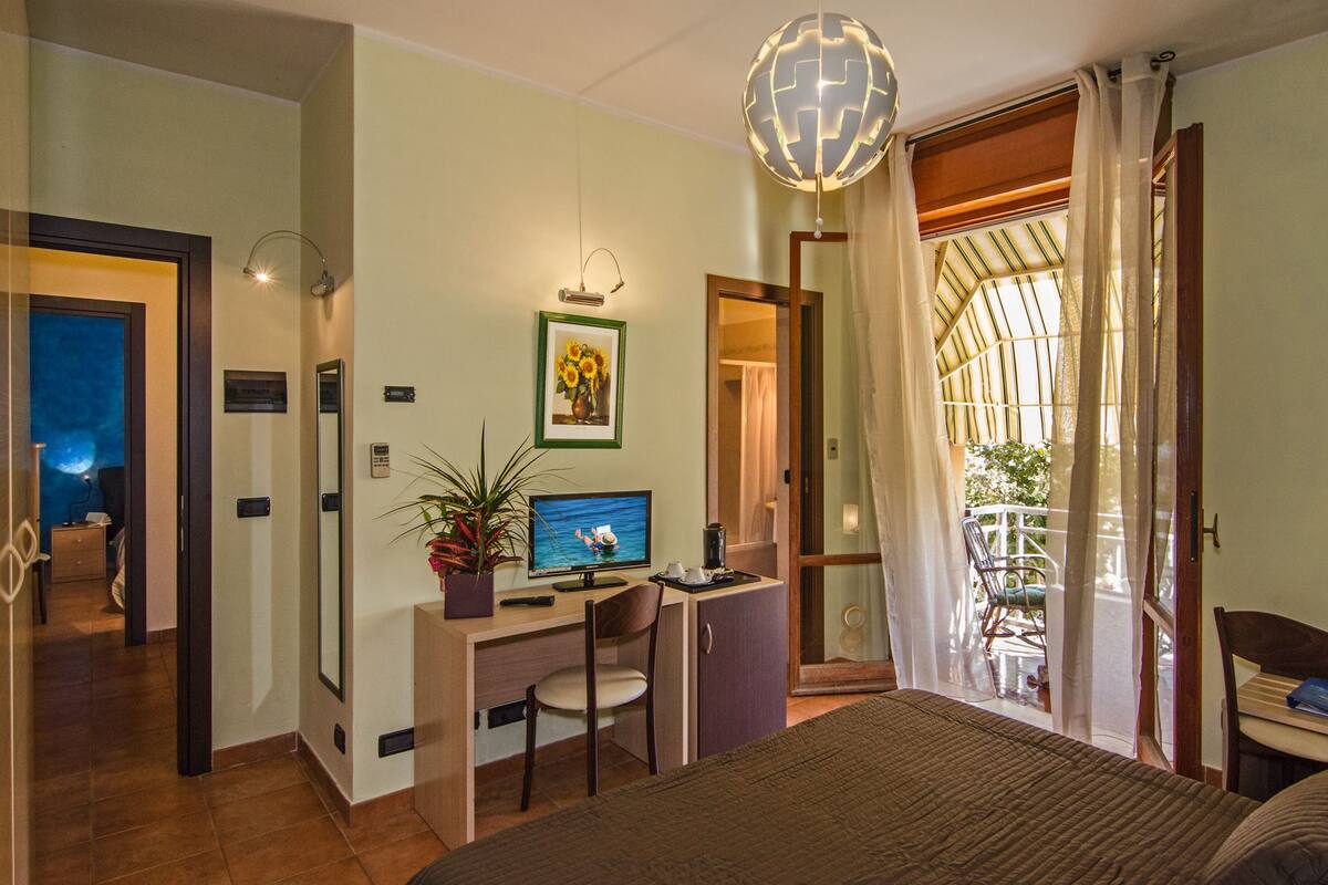 Ein Schlafzimmer mit Bett, Schreibtisch, Stuhl und Blick ins Freie.