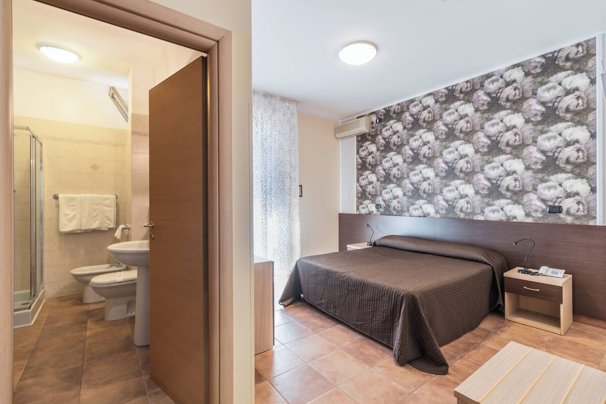Ein Schlafzimmer mit einem großen Bett, einem Nachttisch mit Lampe und einer Wand mit floralem Wandpapier.