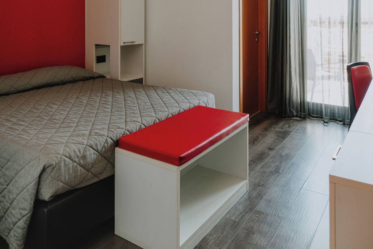 Ein modernes Schlafzimmer mit einem Bett, einer roten Bank, einem Kleiderschrank und einem Fenster mit Vorhängen.