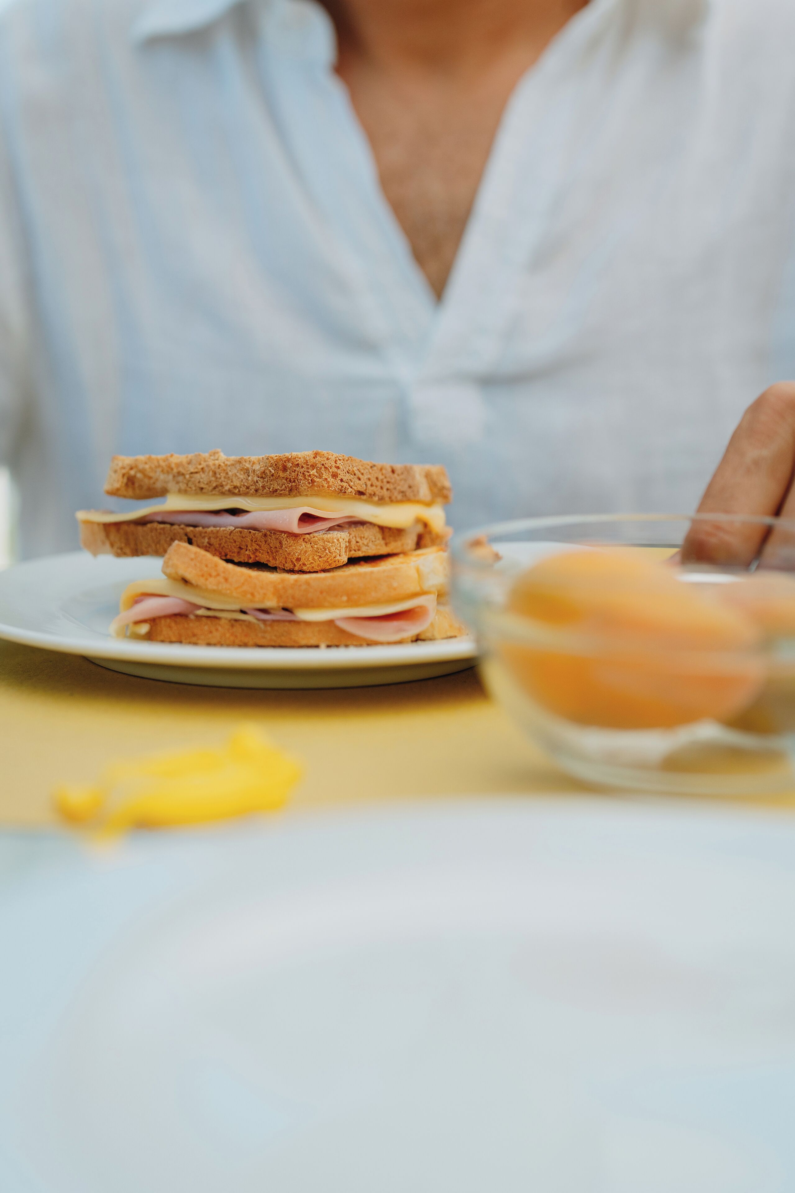 A sandwich on a plate with a bowl of eggs nearby.