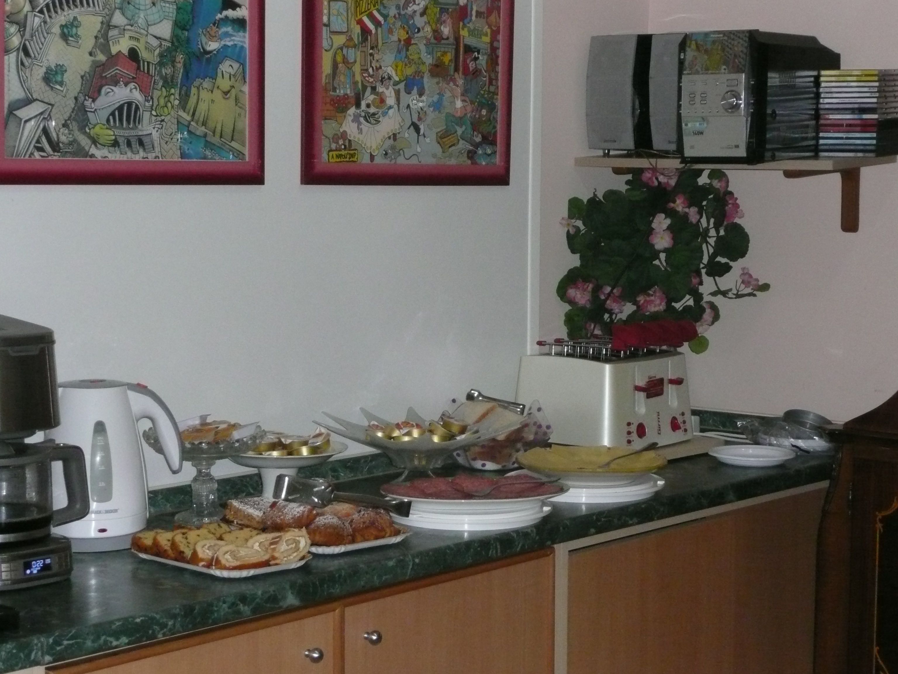 A kitchen counter with a coffee maker, plates of food, and a flower vase.
