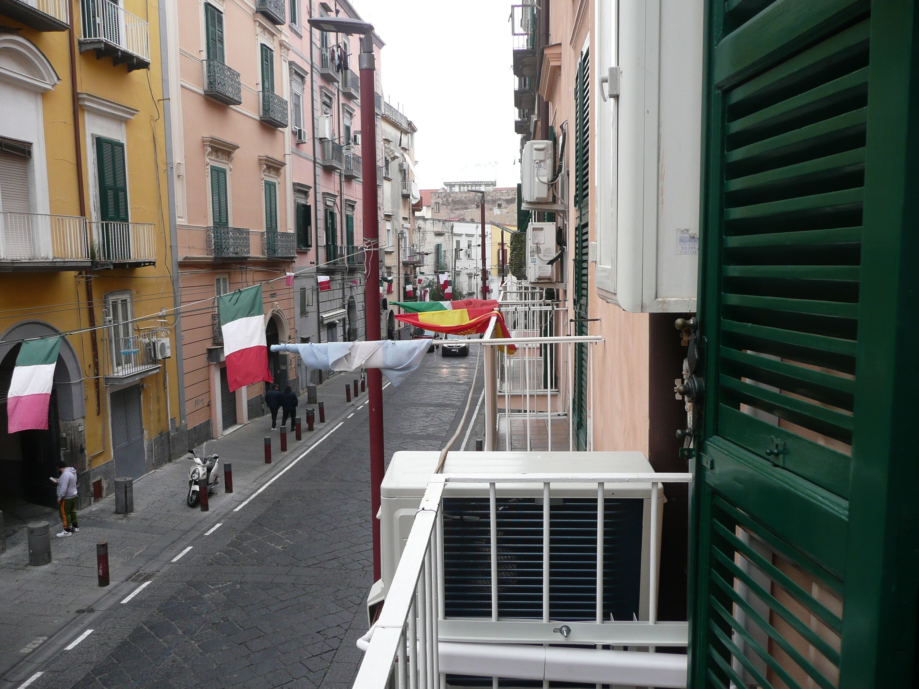 Une rue étroite bordée de bâtiments des deux côtés, avec des balcons et des unités de climatisation.