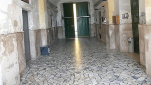 A corridor with a tiled floor, a green door at the end, and a trash bin to the left.
