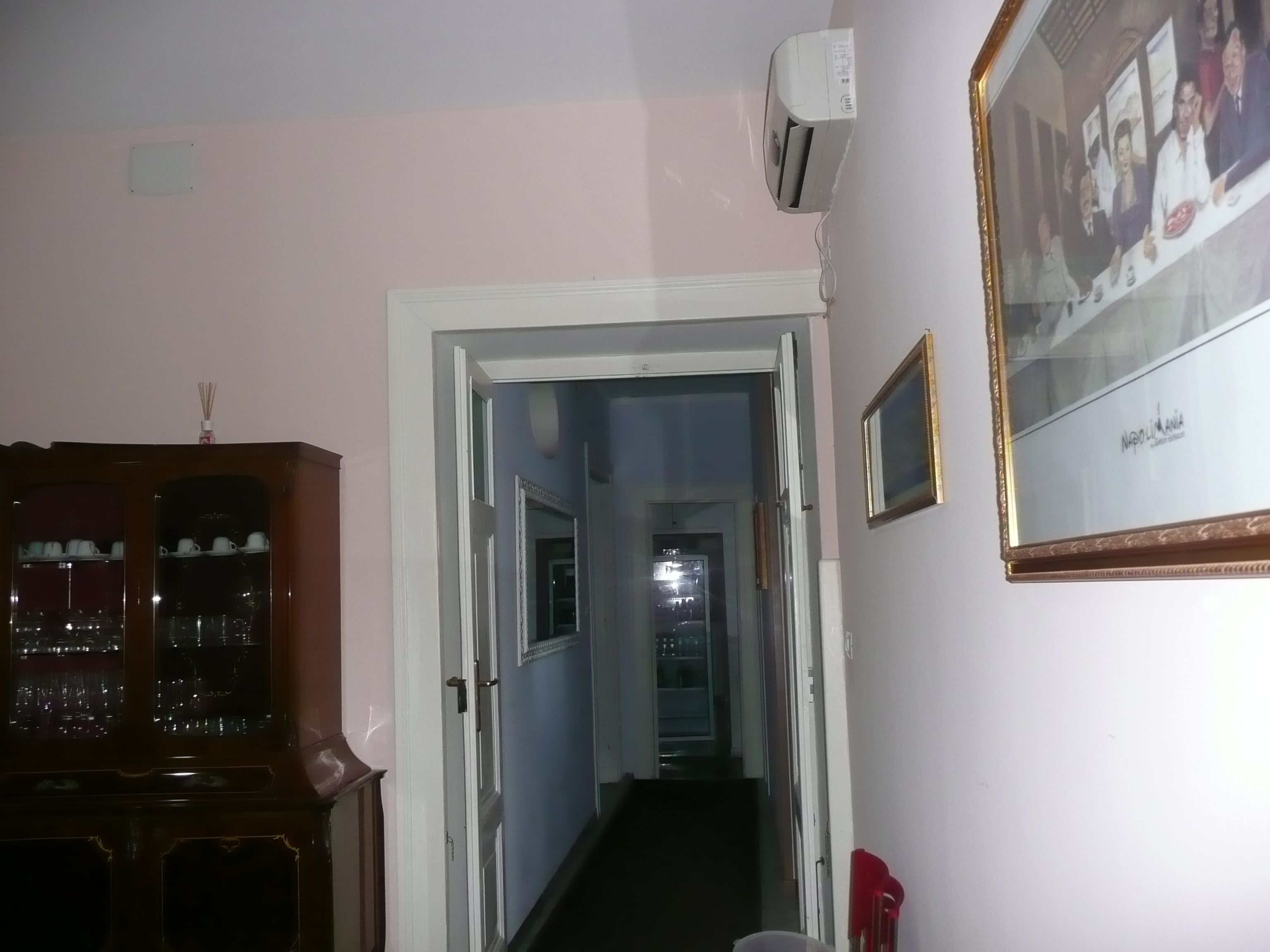 Ein Flur mit einem Holzkasten auf der linken Seite, einer Tür zu einem anderen Raum und einem gerahmten Bild an der Wand.