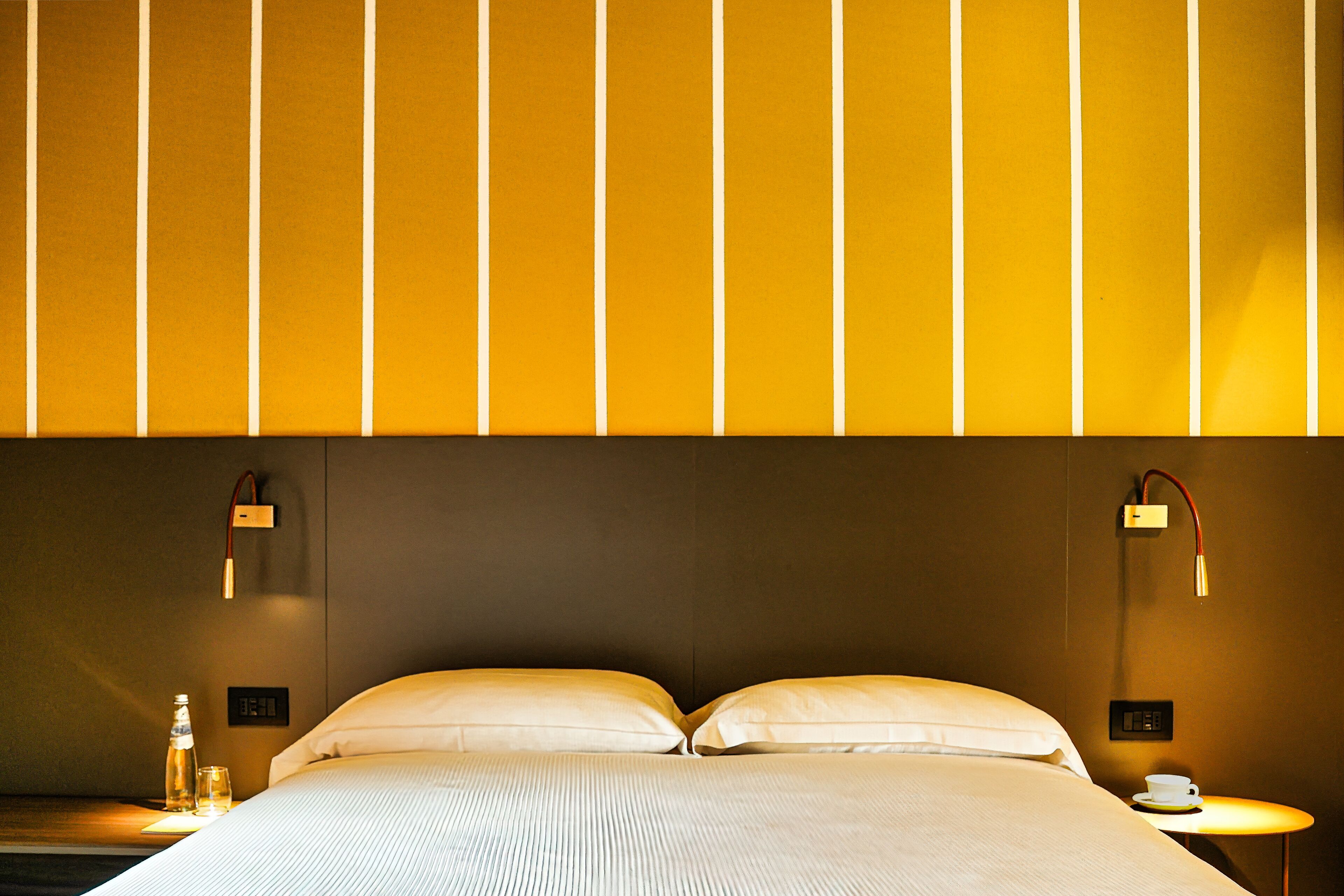 Une chambre d’hôtel avec un grand lit, deux tables de chevet, une petite table et un luminaire fixé au mur.