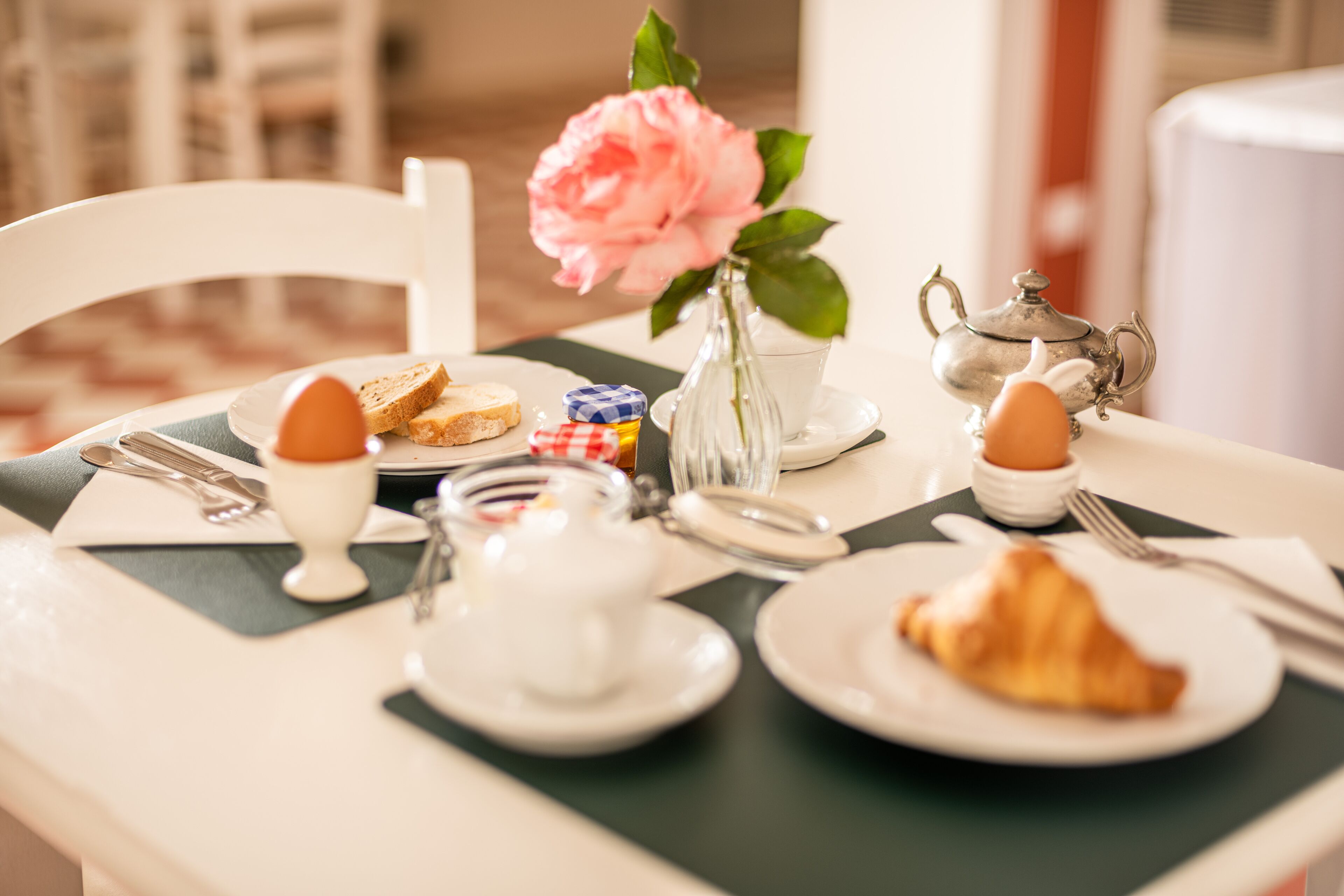 Ein Frühstückstisch mit Teekanne, Tassen, Tellern und einer Vase mit einer Blume.