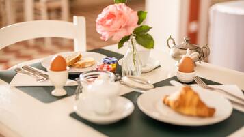 Ein Frühstückstisch mit Teekanne, Tassen, Tellern und einer Vase mit einer Blume.