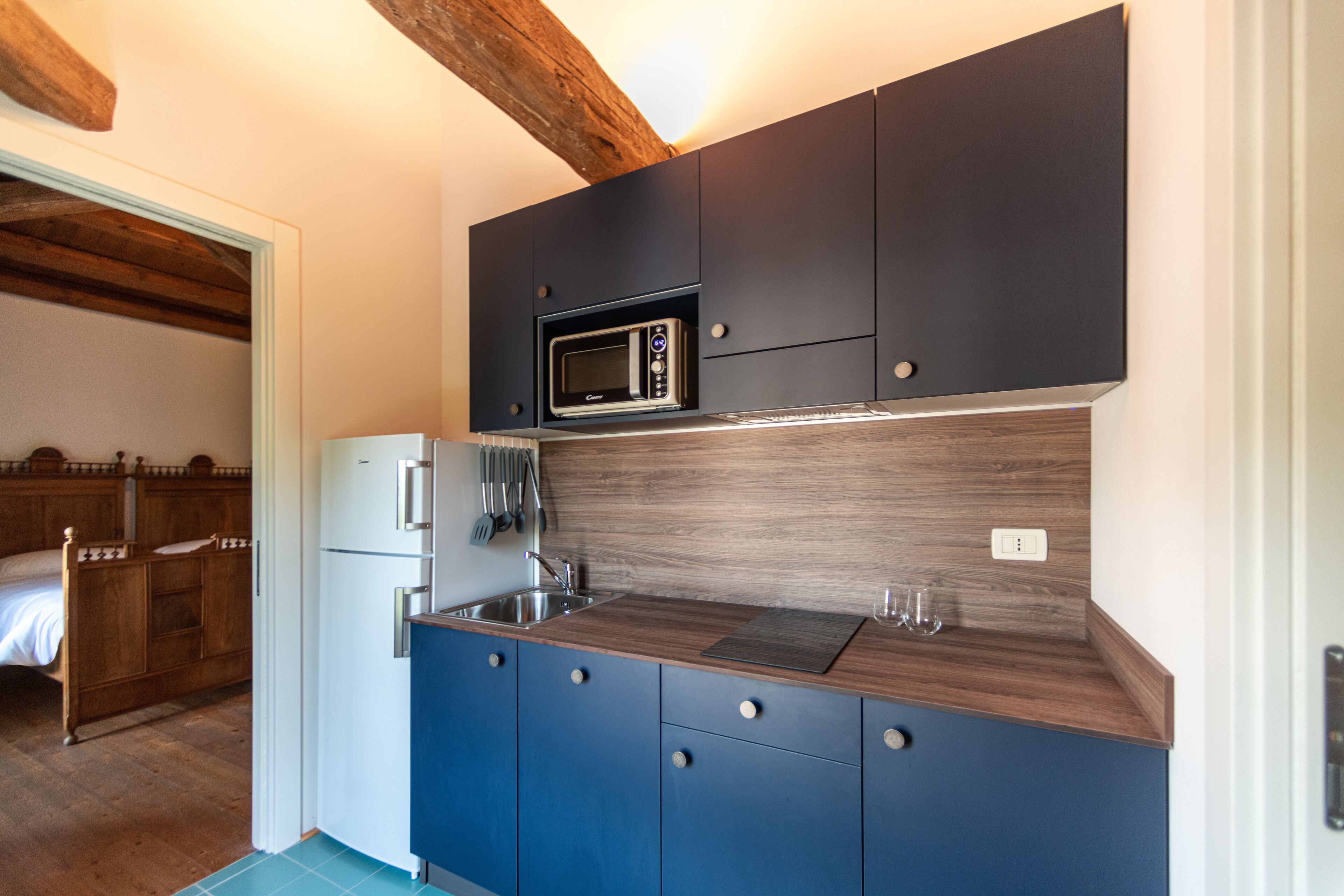A compact kitchen with dark blue cabinets, a microwave, a sink, and a refrigerator.
