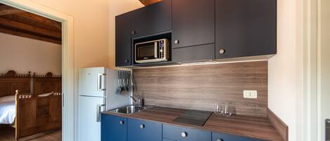 A compact kitchen with dark blue cabinets, a microwave, a sink, and a refrigerator.