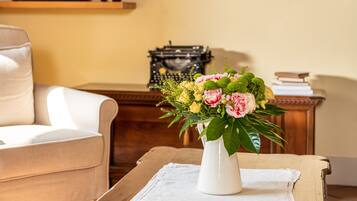 Una sala de estar con un sofá, una mesa de centro con un libro y un jarrón de flores, un televisor y cuadros en la pared.