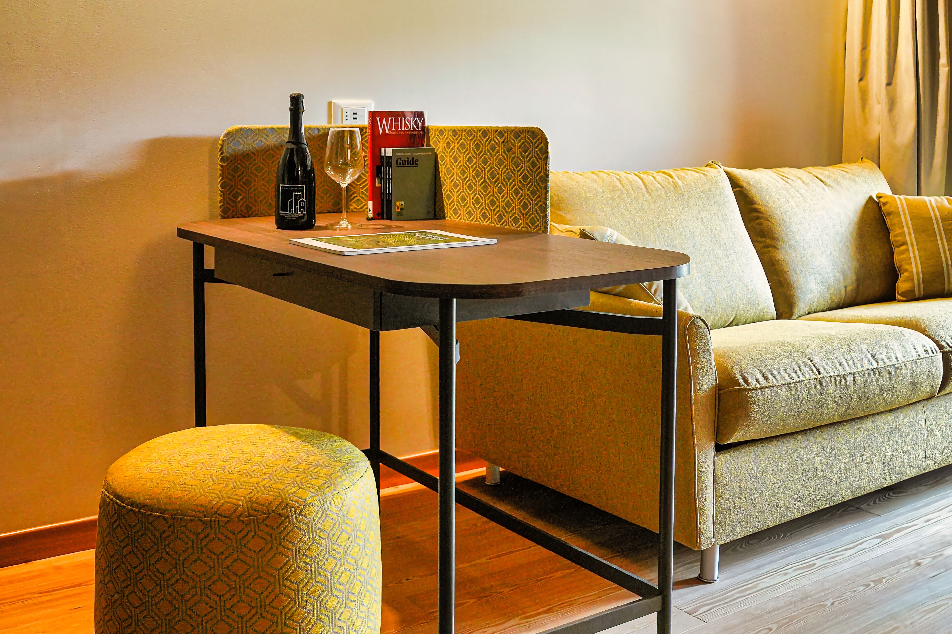 A small, cozy room with a sofa, a wooden table, and a patterned ottoman.