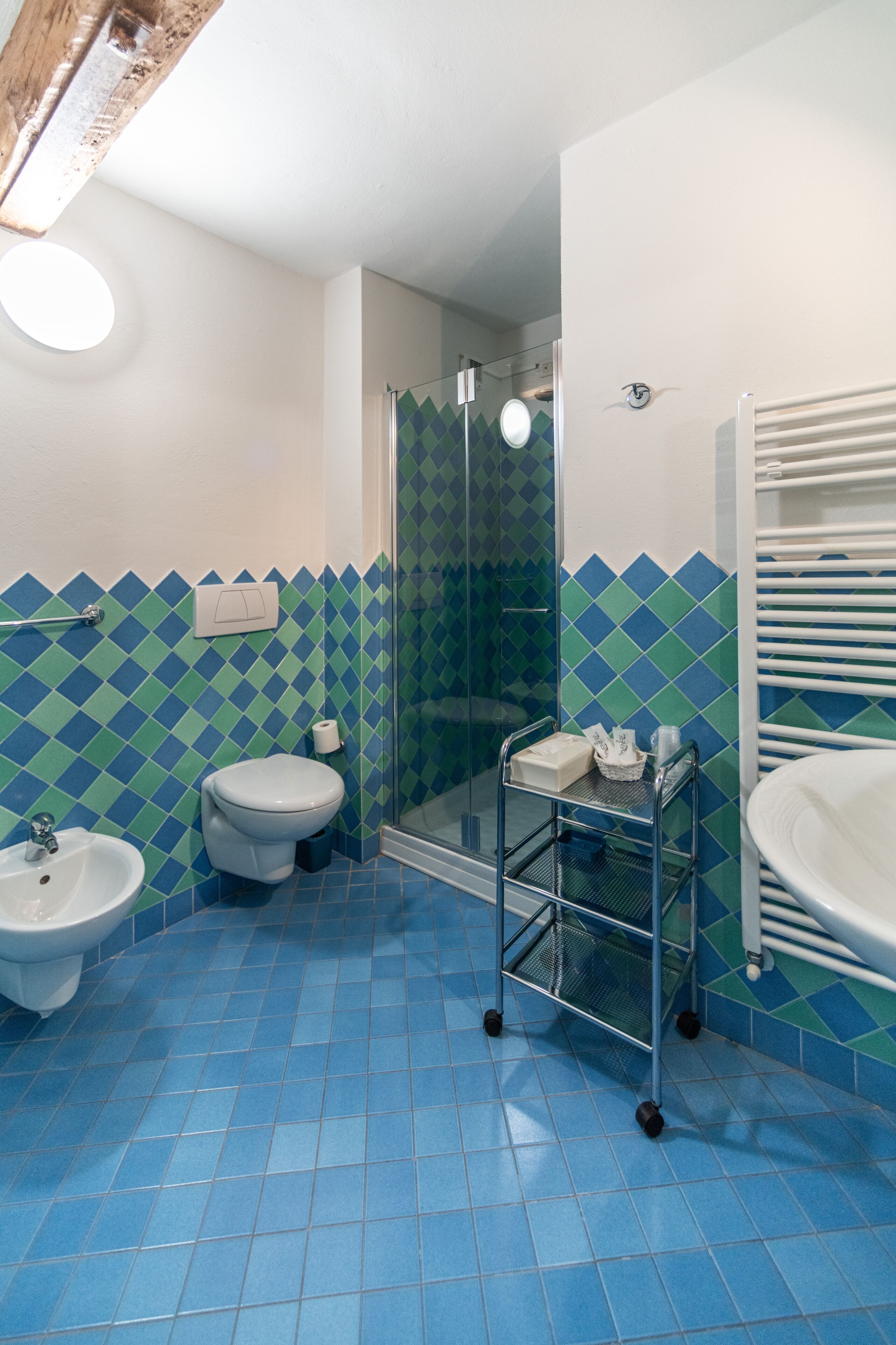 Un baño con piso de azulejos azules, inodoro y lavamanos blancos, y cabina de ducha con mampara de vidrio.