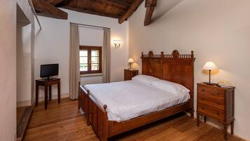 A bedroom with a wooden bed, two bedside tables with lamps, a television on a side table, and a window with curtains.