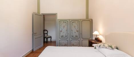 A bedroom with a bed, a chair, a wardrobe, and a nightstand with a lamp.