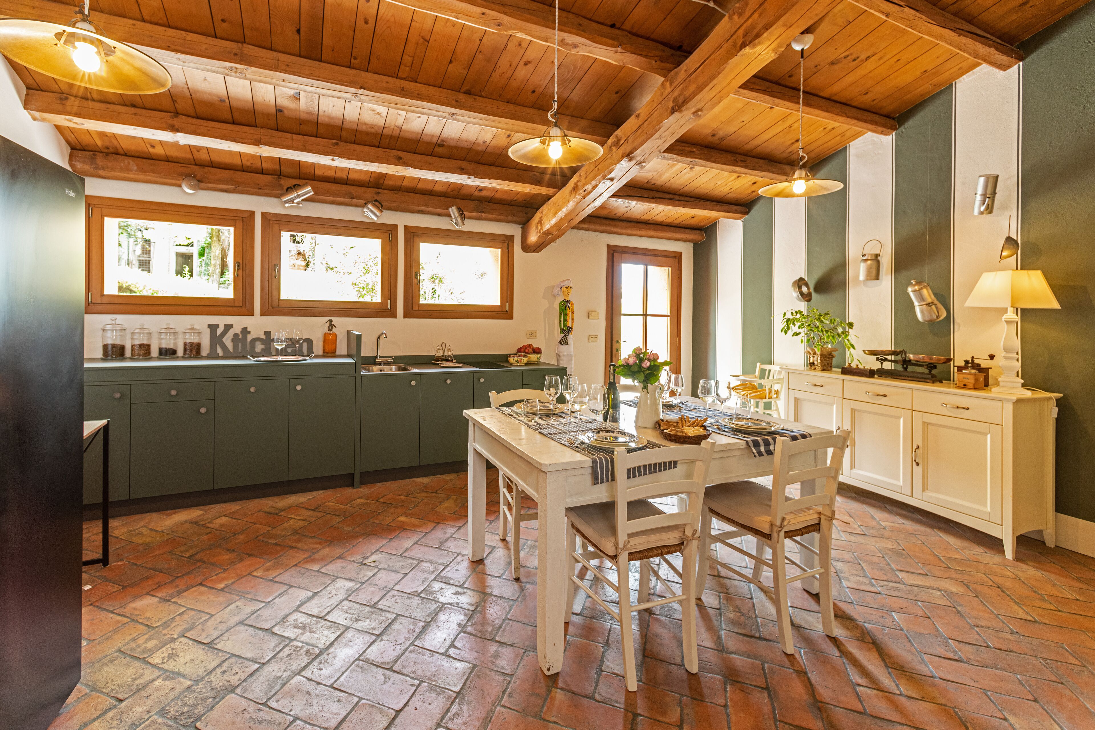 Una cocina con vigas de madera, armarios verdes y suelo de ladrillo.