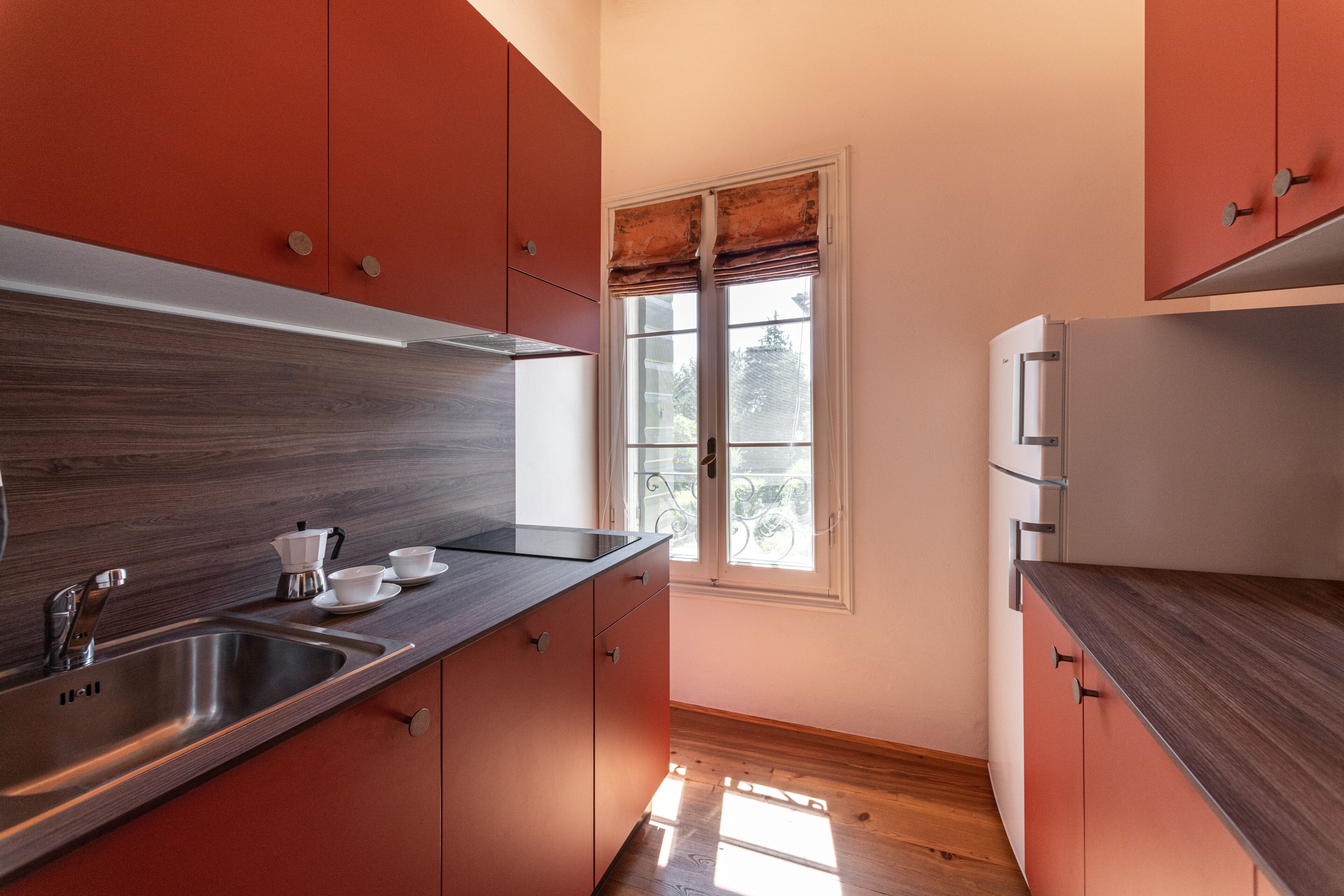 Cocina compacta con pileta de acero inoxidable, cubierta de madera y muebles color rojo.