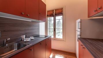 Cocina compacta con pileta de acero inoxidable, cubierta de madera y muebles color rojo.