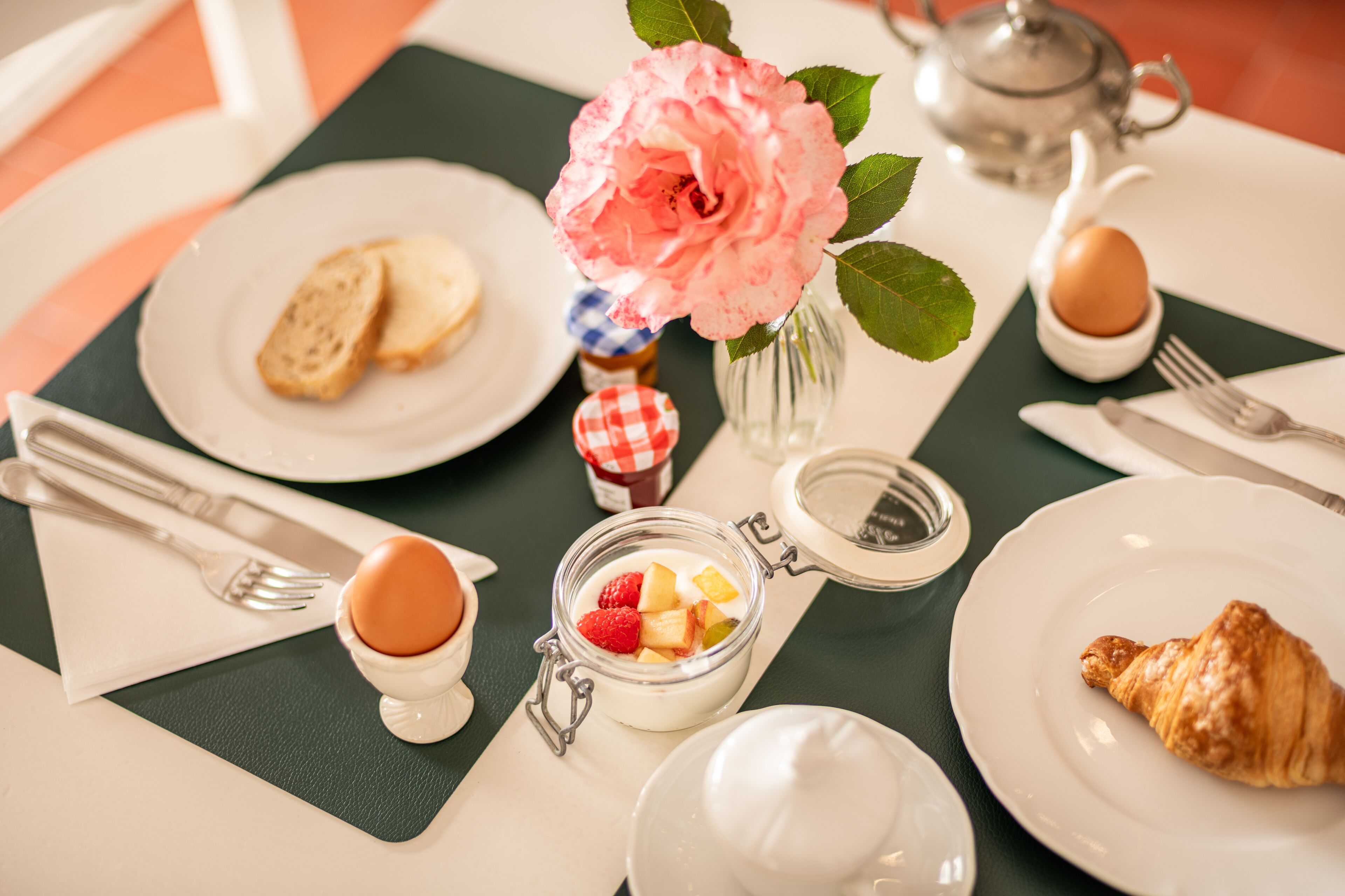 A table set with plates, a teapot, a jar of fruit, and a croissant.