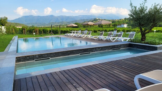 A swimming pool with lounge chairs and a wooden deck, surrounded by greenery and mountains in the background.