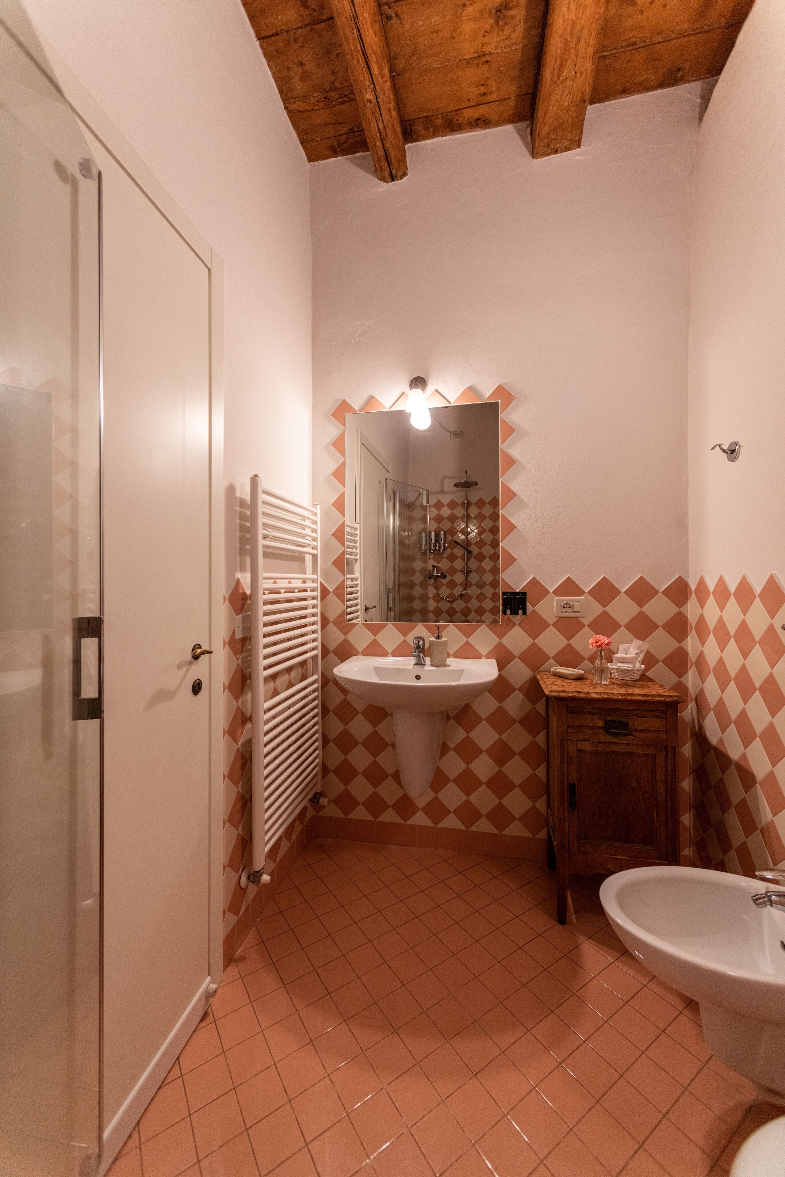 Un bagno con una porta bianca, un lavandino, uno specchio e un mobiletto in legno.