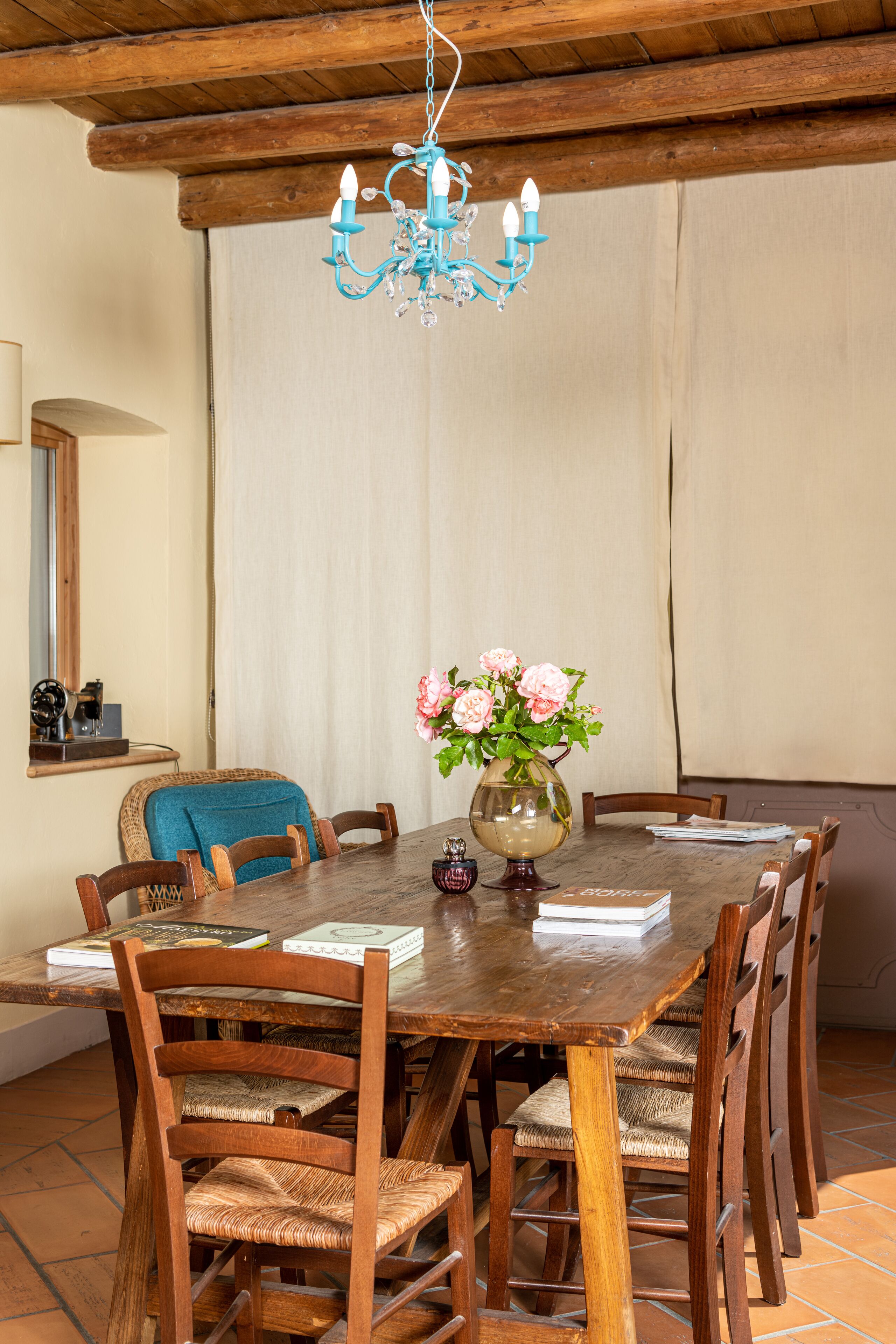 A wooden dining table surrounded by chairs, a chandelier, and a vase with flowers.