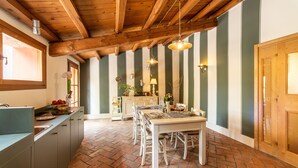 A kitchen with a brick floor, wooden ceiling beams, and a dining area with a table and chairs.