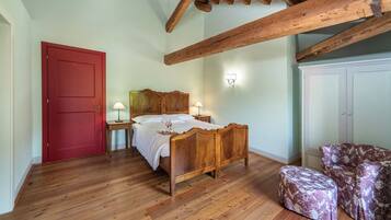 Een slaapkamer met een houten bed, een rode deur, een nachtkastje met een lamp, een gestreept poef en een garderobe.