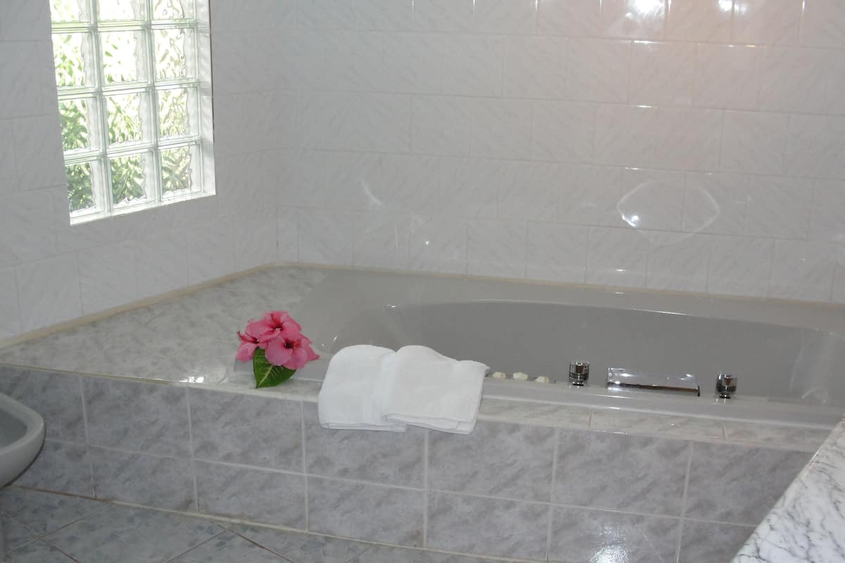 A bathroom with a marble-tiled floor, a bathtub, and a window with a view of greenery.