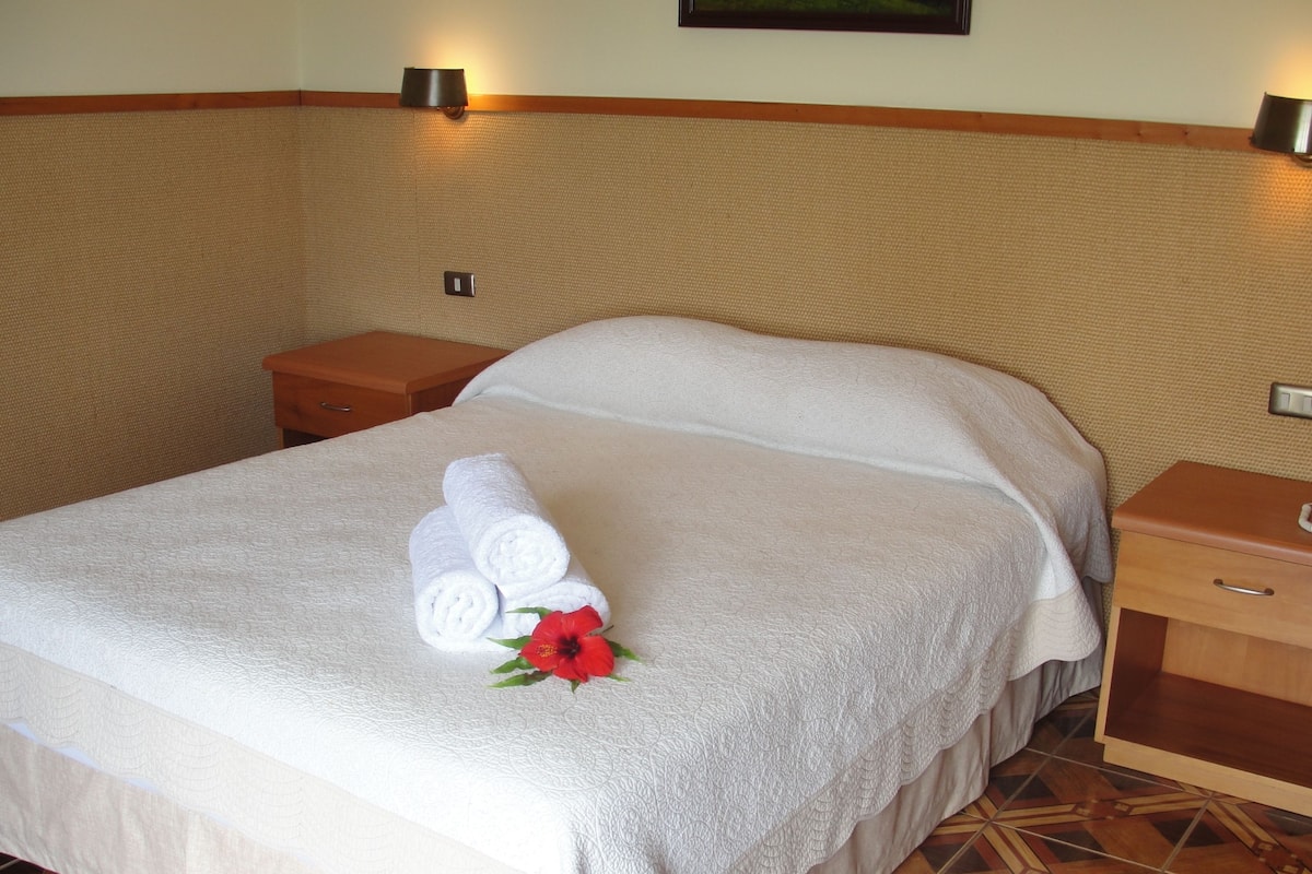 A neatly made bed with white linens and a red flower decoration, wooden nightstands, and a patterned floor.