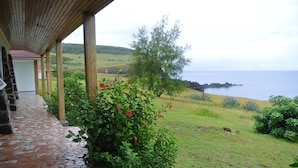 A covered patio with a mosaic floor, a view of the sea, and a grassy area with plants. - Iorana Hotel (Hanga Roa)