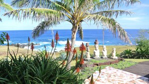 A tropical garden with a palm tree, red flowers, and a view of the ocean. - Iorana Hotel (Hanga Roa)