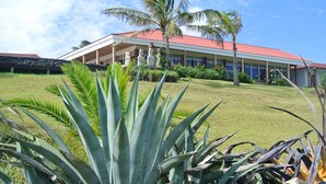 A building with a red roof, surrounded by tropical plants and a clear sky. - Iorana Hotel (Hanga Roa)