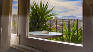 Un balcón con una mesa redonda y un cenicero blanco, con vistas a un paisaje urbano y montañas.