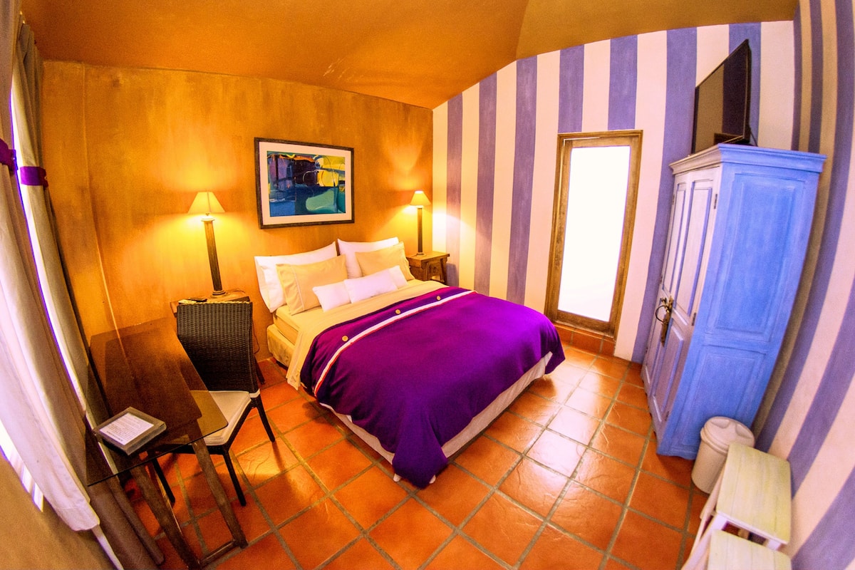 A bedroom with a bed, two bedside tables, a chair, a wardrobe, and a painting on the wall.