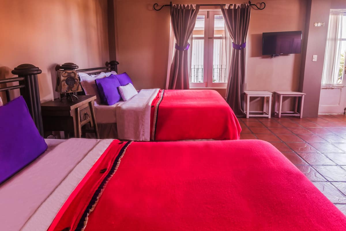 A hotel room with two beds, a desk, a chair, a television, and a window with curtains.
