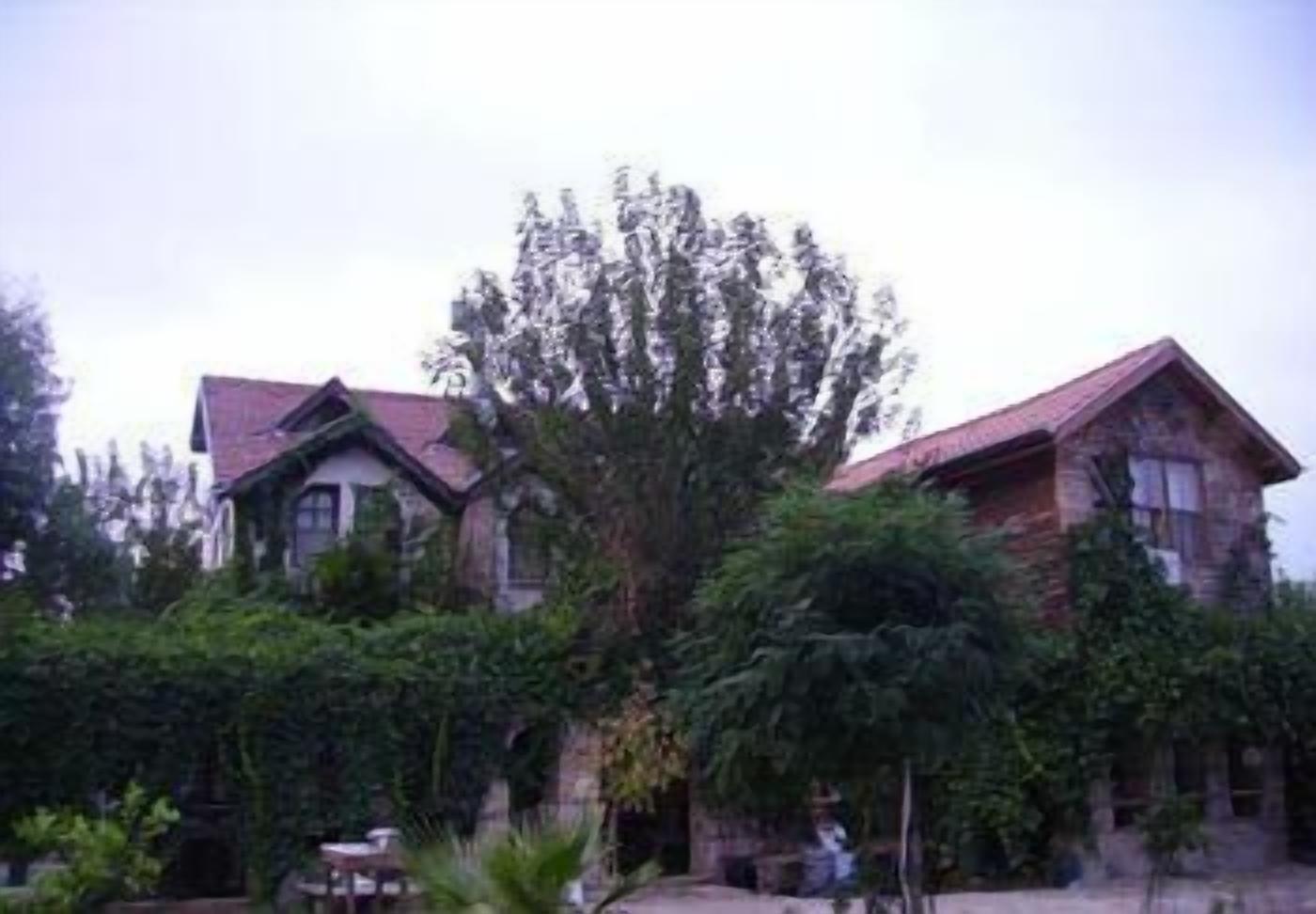 Un edificio de dos pisos con techo rojo y fachada de piedra, rodeado de abundante vegetación.