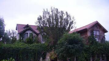 Un edificio de dos pisos con techo rojo y fachada de piedra, rodeado de abundante vegetación.