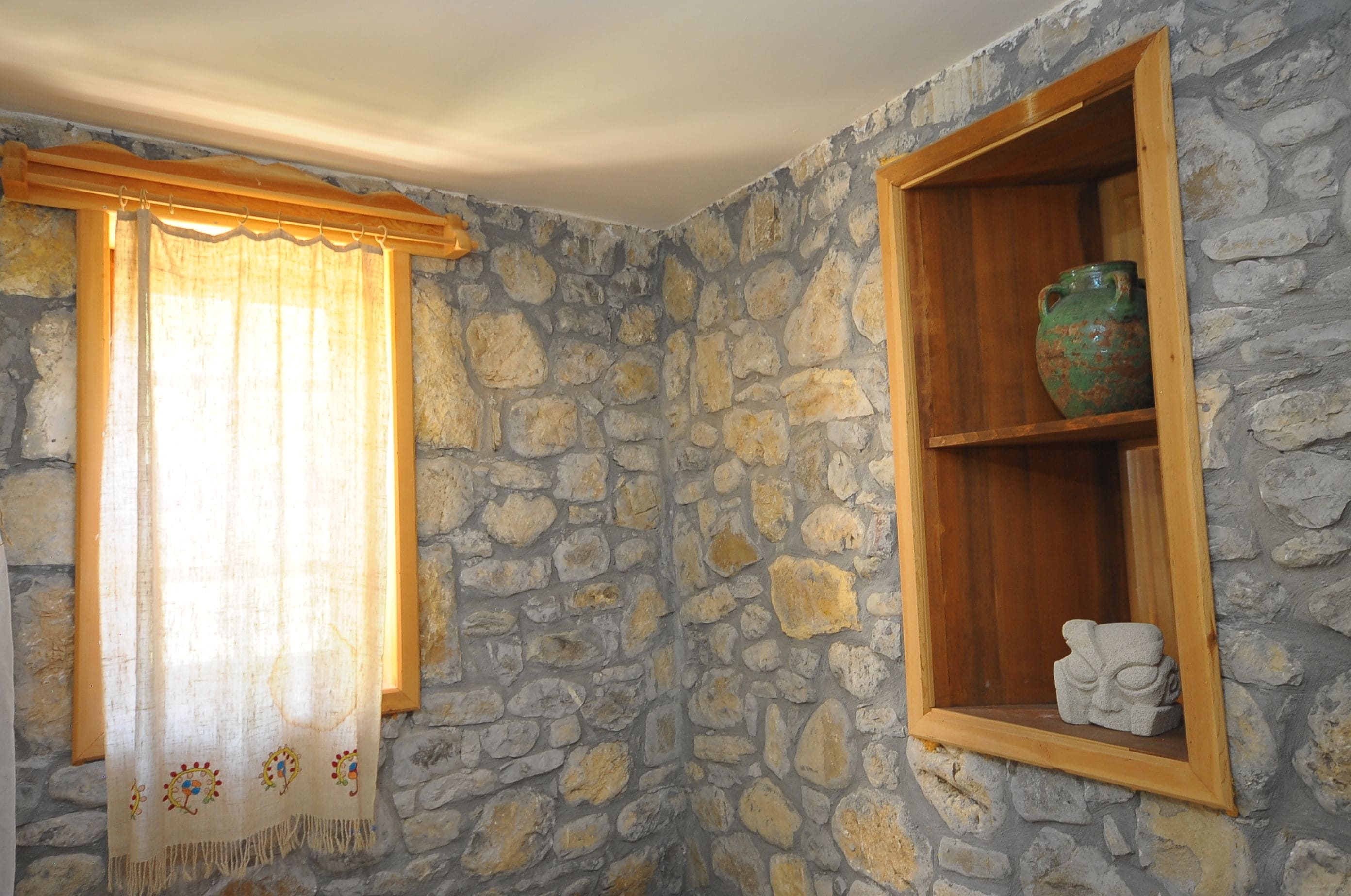 Un muro in pietra con una finestra, una tenda e uno scaffale con un vaso e una scultura.