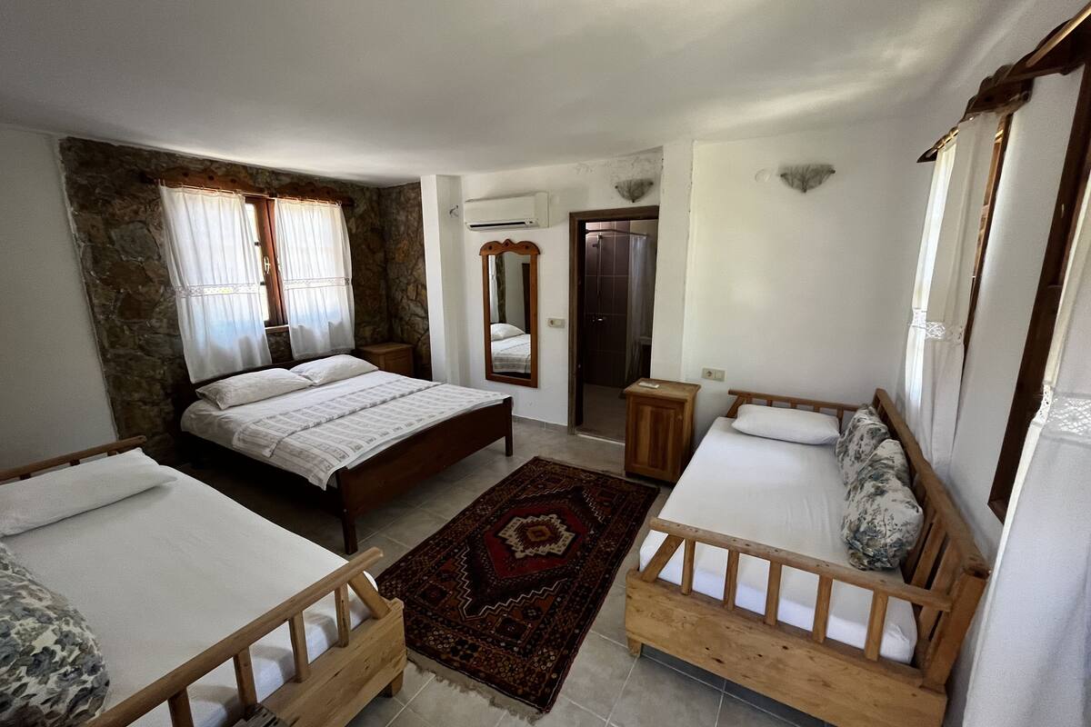 A bedroom with a large bed, two smaller beds, a wooden headboard, a stone wall, a mirror, and a shower area.