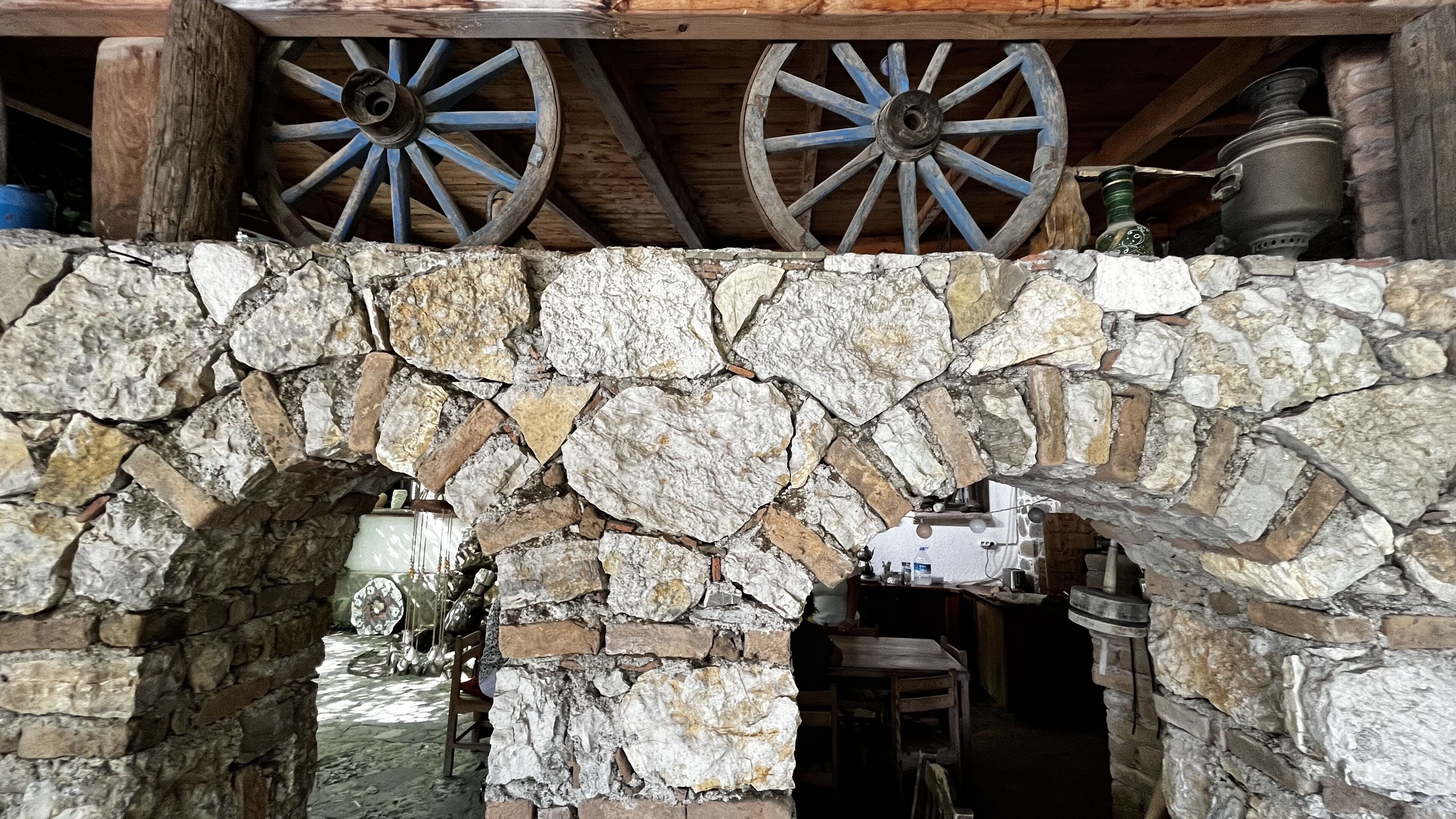Un arco de piedra que da paso a un interior rústico con vigas de madera y un carro de madera con ruedas azules.