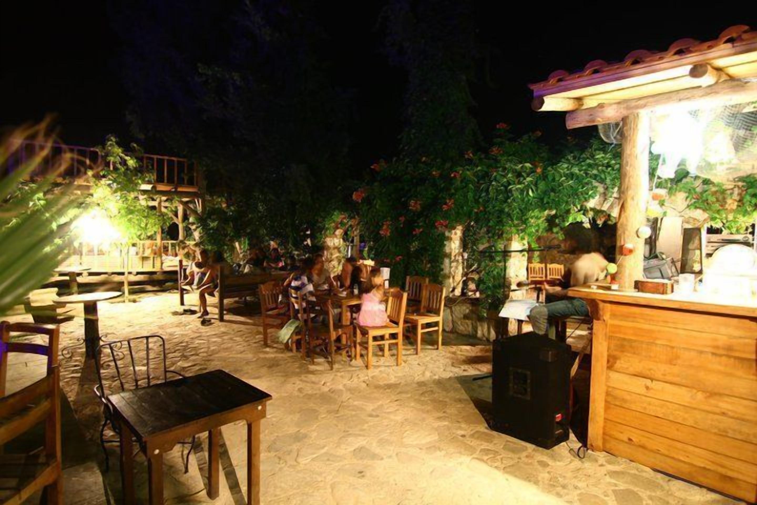 An outdoor patio area with stone flooring, wooden tables and chairs, and a small bar area with a light fixture.