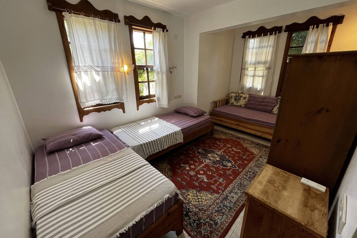 A small, cozy room with two single beds, a bench, and a large rug.