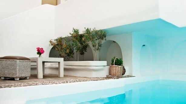 Una zona junto a la piscina con un banco blanco, un otoman de mimbre y plantas en macetas.