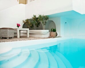 A poolside area with a white bench, wicker ottoman, and potted plants. - Altana Boutique Hotel (Tinos)