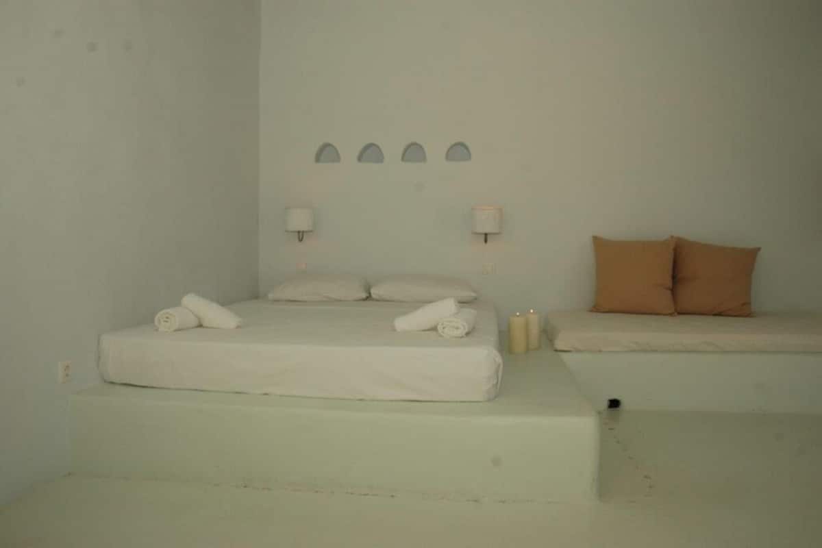 A simple, clean room with a bed, two pillows, a small bench, and wall-mounted lights.