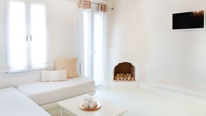Un salón minimalista con un sofá blanco, una mesita con velas, una chimenea y un televisor montado en la pared.