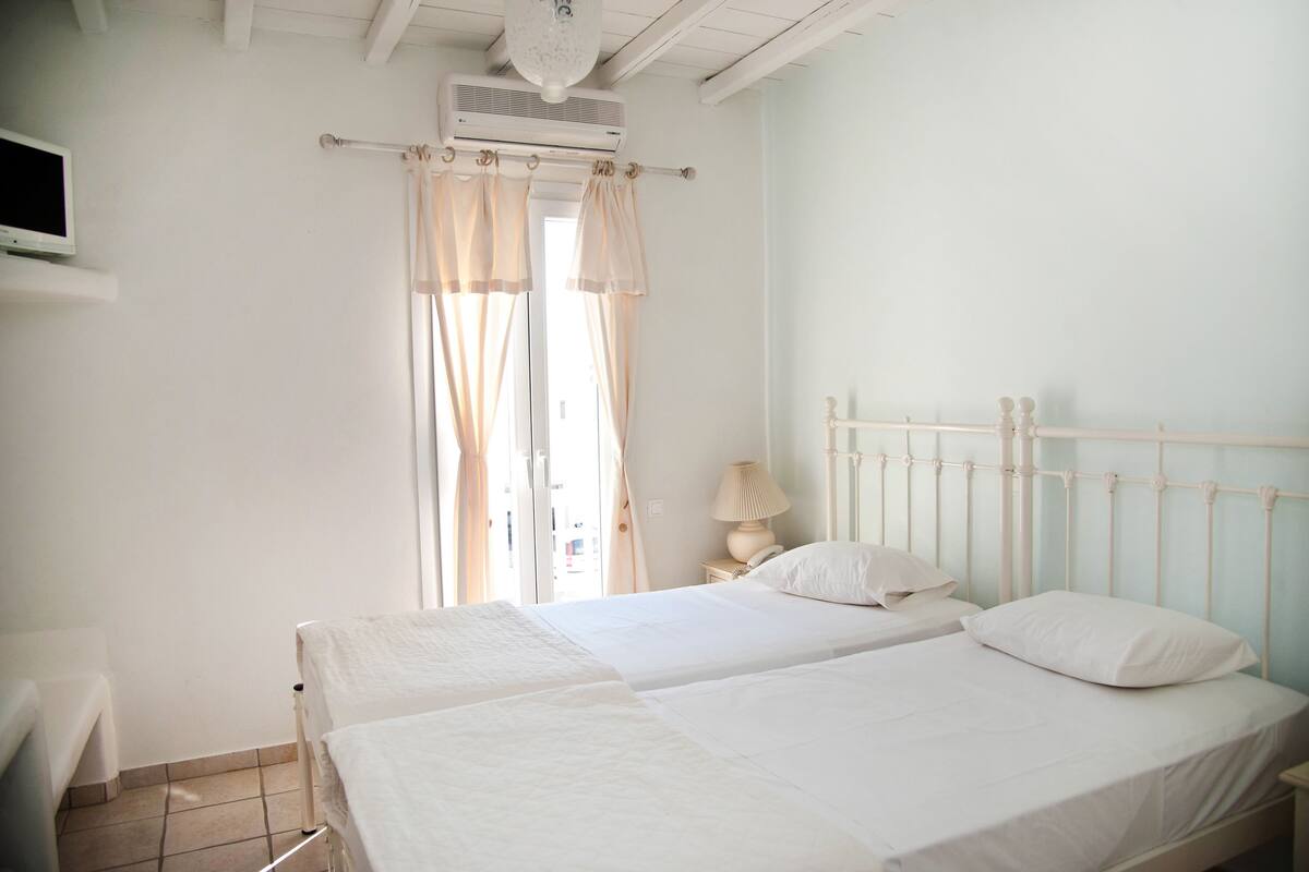 A bedroom with two beds, a TV, and a window with curtains.