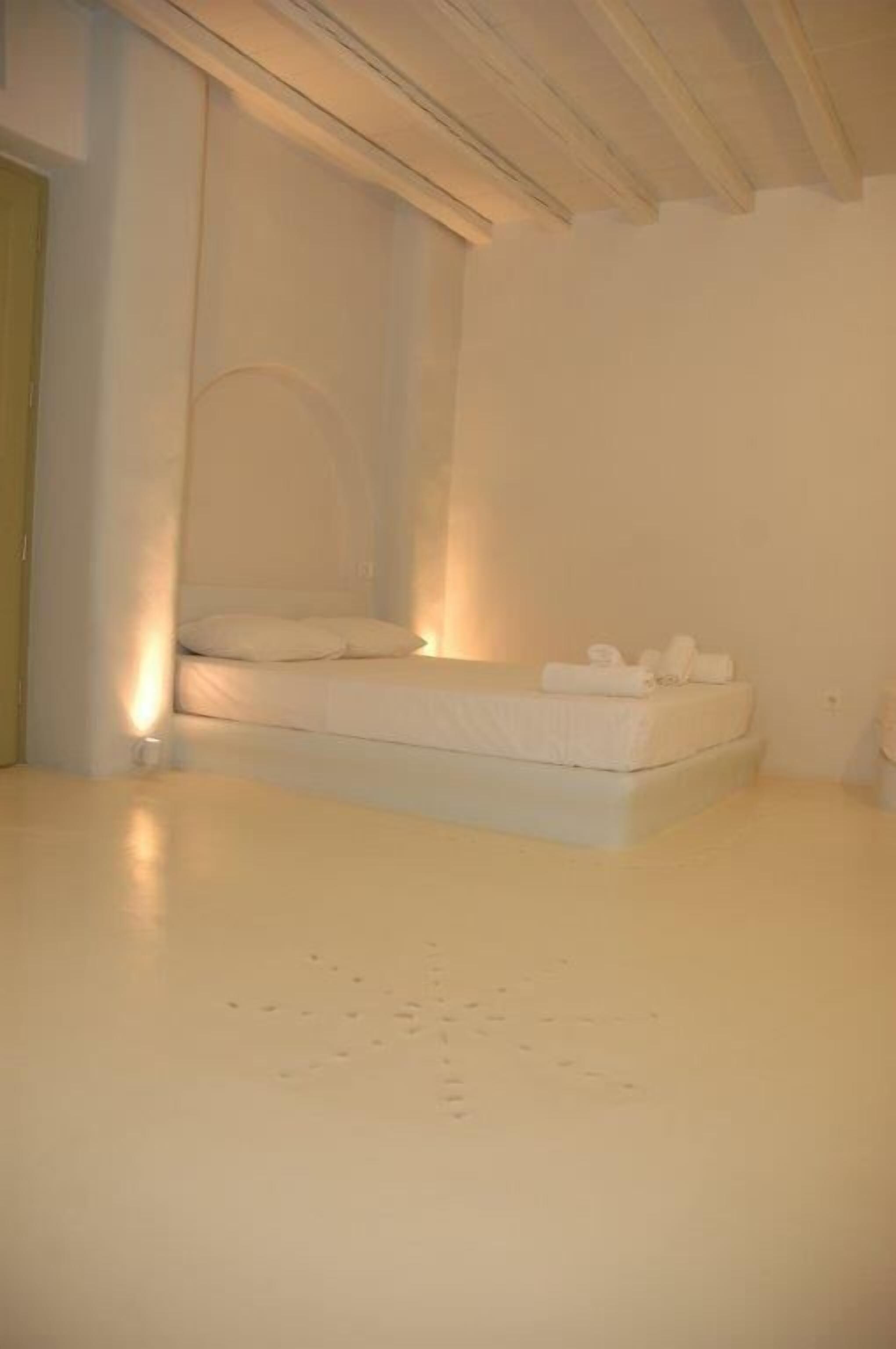 A minimalist room with a single bed, a small bedside table, and a wall-mounted light.