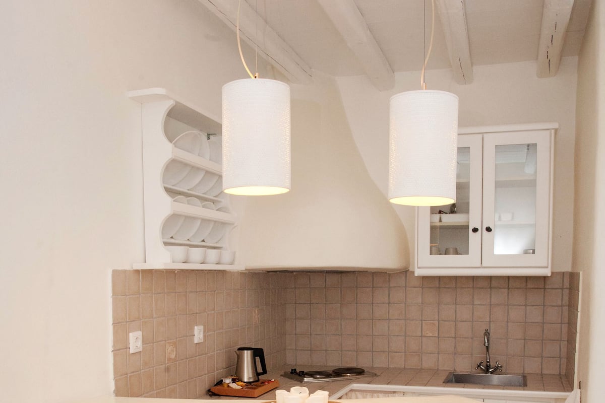 A kitchen with a white countertop, two stools, a sink, and hanging pendant lights.